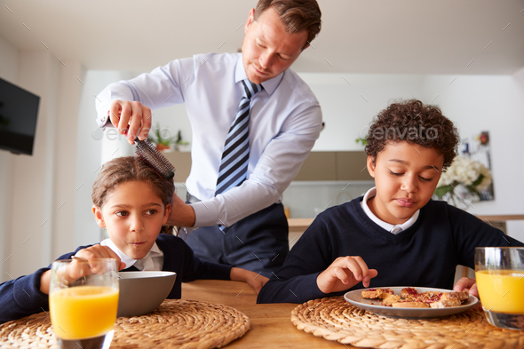 Businessman Father In Kitchen Brushing Hair And Helping Children With Breakfast Before School