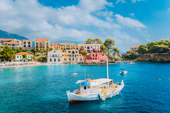 View of beautiful bay of Assos village with fishing boat at anchor in front and clouds in background - Stock Photo - Images