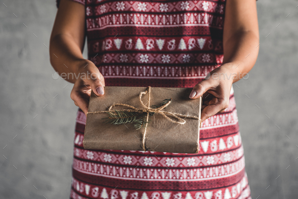 Female wearing a red with red christmas dress has a christmas gift in her hands