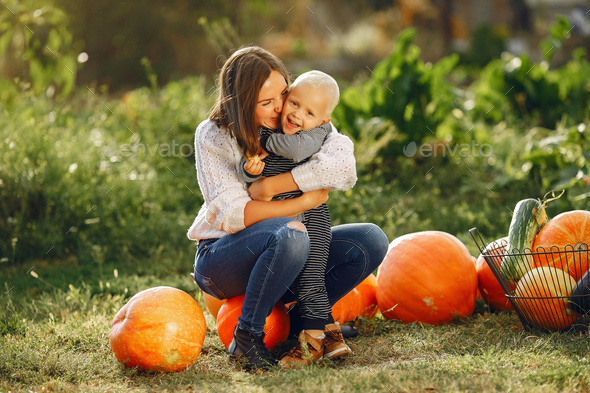 Mother and son sitting on a garden near many pumpkins