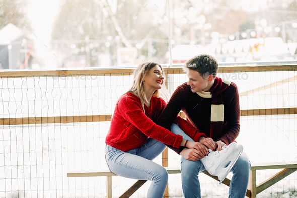 Cute couple in a red sweaters help each other to skate