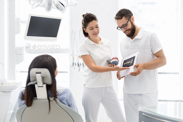 Two cheerful dentists explaining teeth disease treatment to patient - Stock Photo - Images