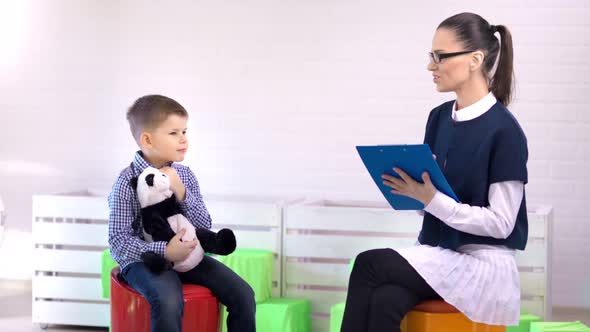 Smiling Female Professional Child Psychologist Talking with Little Boy Medium Long Shot alt