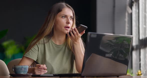 Businesswoman Calling Up with Partner and Adding Information in Paper Diary While Sitting in Cafe alt