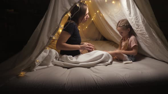 A Happy Mother Does a Foot Massage Her Daughter in a Tent in the Living Room alt