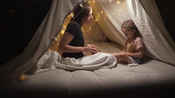 A Happy Mother Does a Foot Massage Her Daughter in a Tent in the Living Room
