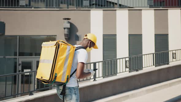 An AfricanAmerican Courier in a Medical Mask Delivers a Package of Food to a alt