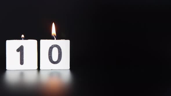 A square candle saying the number 10 being lit and blown out on a dark black background alt