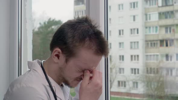 A young doctor is very upset, he is standing near the window
