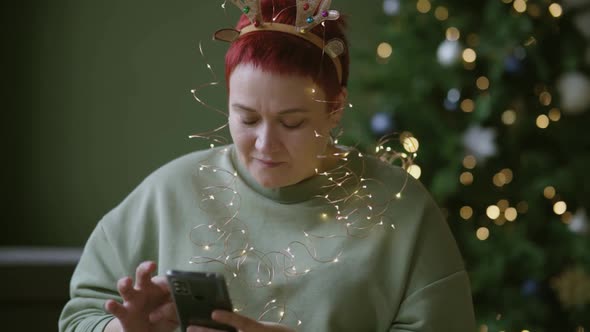 Woman Reads Writes Merry Christmas and Happy New Year Greetings on Smartphone alt