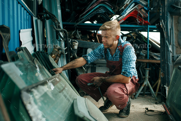 Male repairman choosing glass on car junkyard