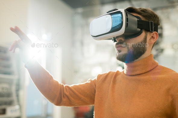 Serious man in vr goggle touching virtual display while making presentation