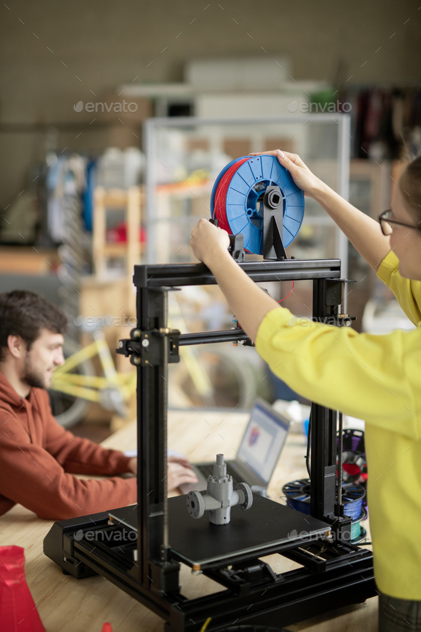 Young woman putting new spool with filament on 3d printer before starting work