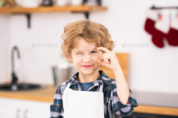 Happy cute little boy in apron holding star shaped cutter by his eye