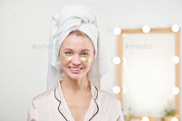 Pretty young smiling female with towel on head having under-eye mask