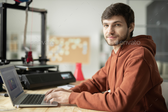Bearded guy in brown hoodie working over sketches of items for 3d prirnting
