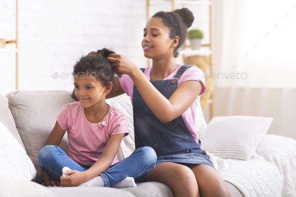 Caring african teenage girl brushing her little sister hair at home