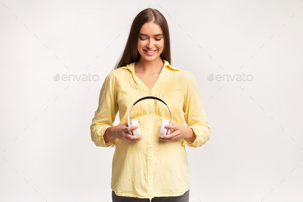 Smiling Pregnant Lady Standing Holding Headphones Near Belly, White Background