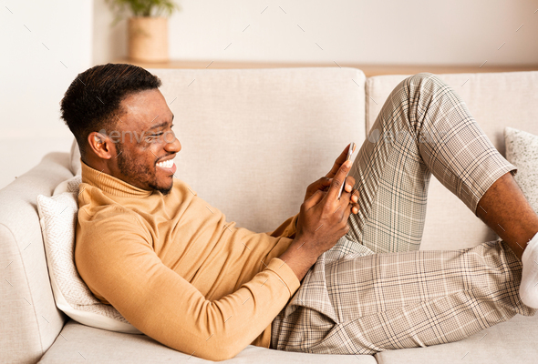 Relaxed Guy Using Smartphone Lying On Sofa At Home