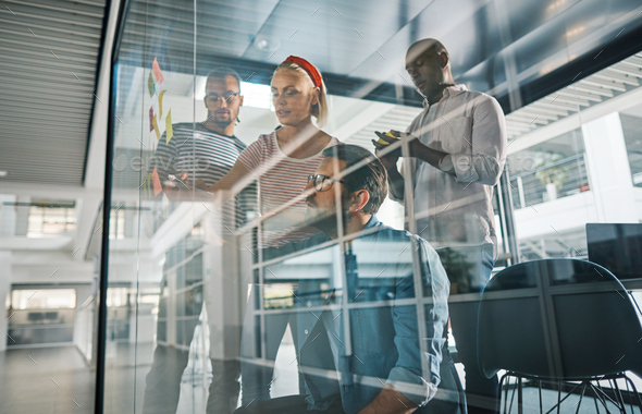 Diverse businesspeople brainstorming on the glass wall of a boardroom - Stock Photo - Images