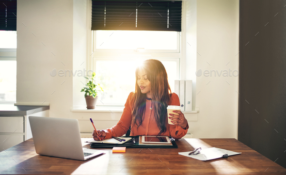 Smiling young female entrepreneur drinking coffee and working at home - Stock Photo - Images