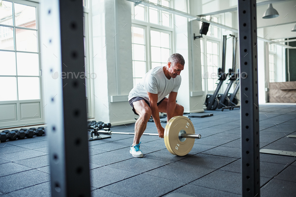 Senior man in sportswear lifting weights alone in a gym