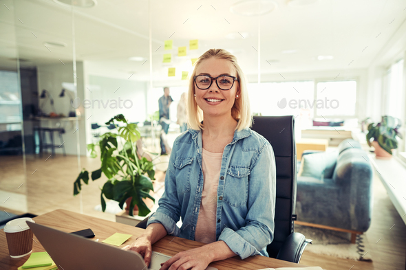 Smiling businesswoman sitting at her desk in an office desk - Stock Photo - Images