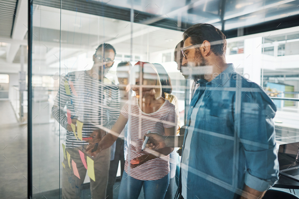 Smiling businesspeople brainstorming with sticky notes on a glass wall - Stock Photo - Images