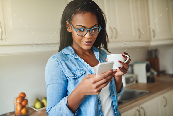 Young African woman drinking coffee and reading text messages - Stock Photo - Images