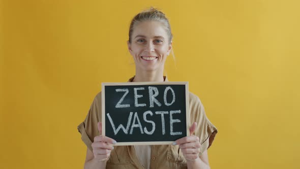 Portrait of Smiling Young Woman Holding Zero Waste Sign on Yellow Background alt
