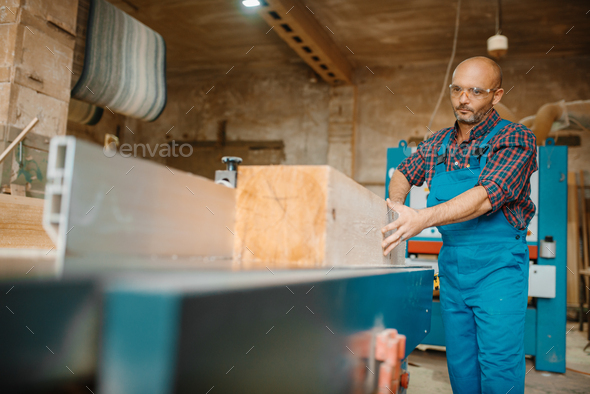 Carpenter processes wooden beam on plane machine - Stock Photo - Images