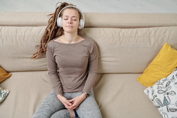 Peaceful young woman with headphones listening to meditation music on couch