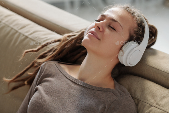 Relaxed girl with headphones smiling while listening to calming music on couch