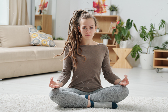 Serene girl in activewear crossing legs while practicing yoga on the floor