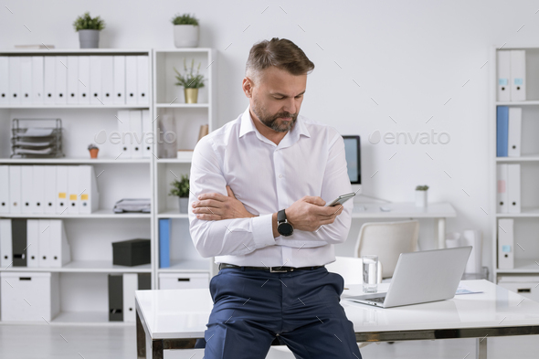 Successful bearded businessman texting or scrolling in smartphone for contact