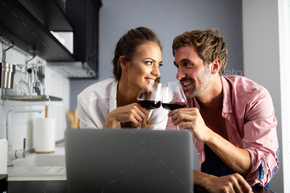 Young couple relaxing in kitchen with wine and laptop. Love, technology, people concept