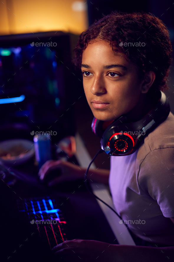 Teenage Girl With Headset Gaming At Home Using Dual Computer Screens