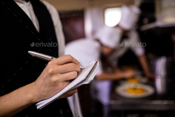 Female waitress noting an order on notepad in kitchen - Stock Photo - Images