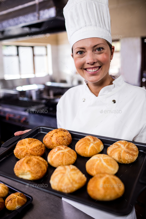 Female chefs holding baking tray of kaiser rolls in kitchen Stock Photo