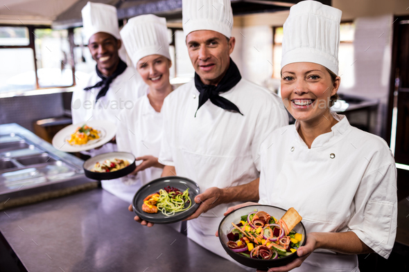 Group of chefs holding plate of prepared food in kitchen