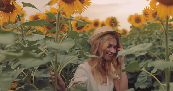 Beautiful Girl in a Hat Flirts and Smiles Near Sunflowers