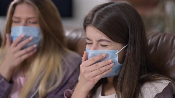 Closeup Ill Woman Coughing with Blurred Roommate in Coronavirus Face Mask at Background alt