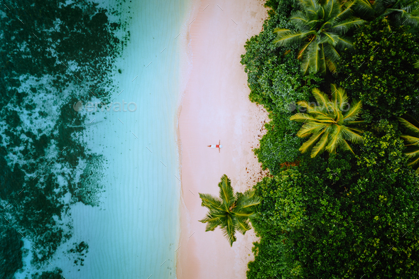 Aerial view of a young woman relaxing on the tropical paradise sandy beach surrounded by palm trees - Stock Photo - Images