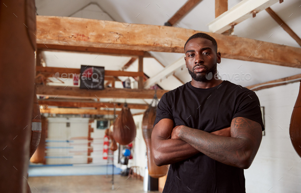 Portrait Of Male Boxer In Gym Standing By Old Fashioned Leather Punch Bag