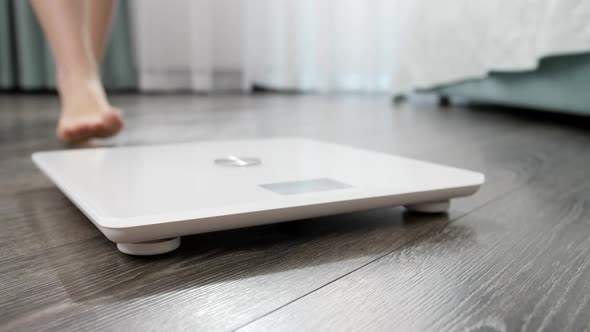 Closeup of Bare Female Feet Standing on Digital Scales on Wooden Floor at Bedroom alt
