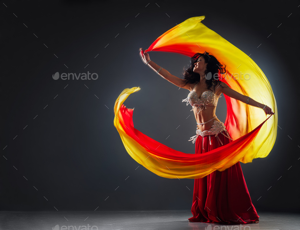 girl in a red ethnic dress on the stage dances oriental dancing waving fabric