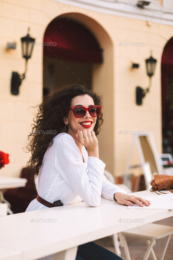 Beautiful smiling in sunglasses standing and happily looking in camera in summer terrace of cafe - Stock Photo - Images