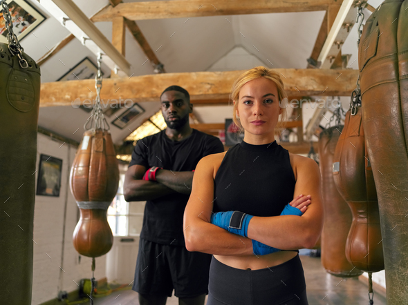 Portrait Of Male And Female Boxers In Gym Training Standing With Leather Punch Bags