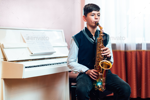 student boy plays saxophone while sitting at a music lesson in class