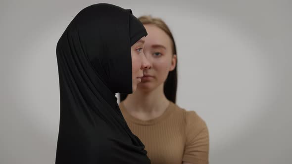 Side View Woman in Hijab Posing at Grey Background with Twin Caucasian Sister at Background alt